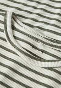 Ribota auduma krekls ar zaļām un baltām horizontālām svītrām. Iekļauj apaļu kakla izgriezumu un mazu zīmola birku netālu no apkakles.