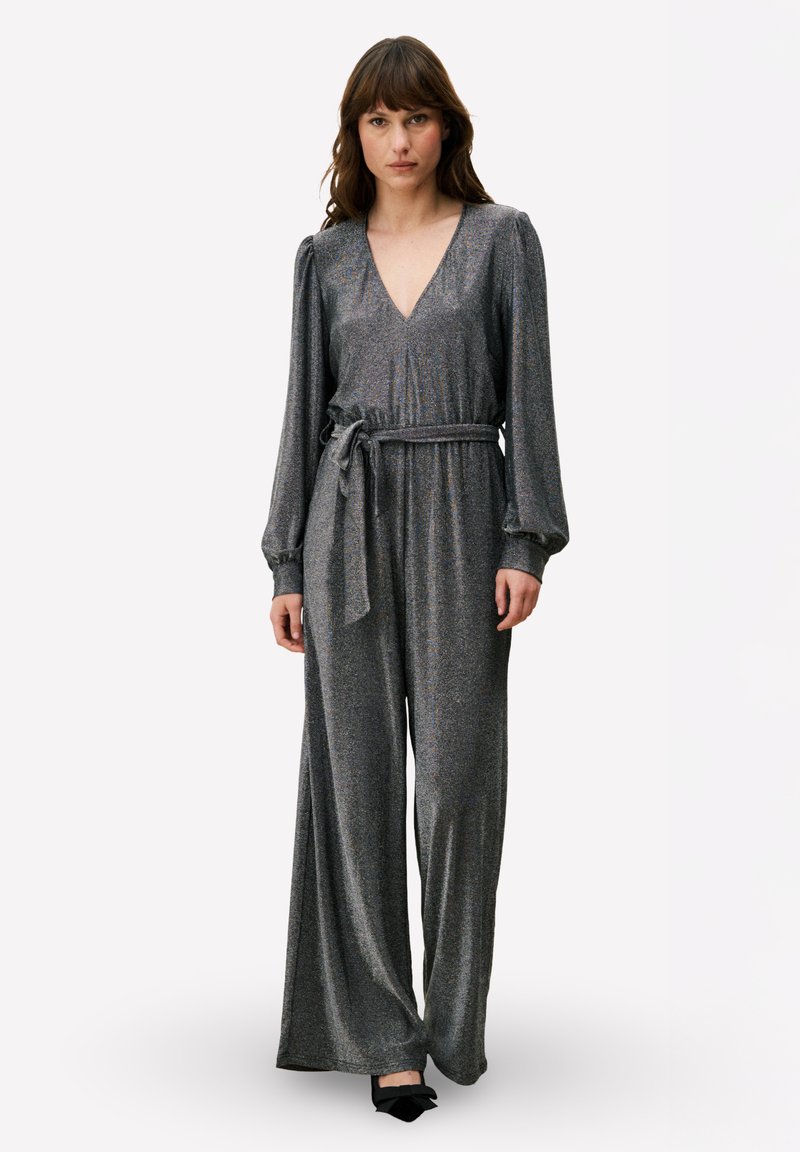 Combinaison grise brillante avec un col en V profond, des manches longues bouffantes, une taille cintrée et des jambes larges, complétée par une ceinture assortie.
