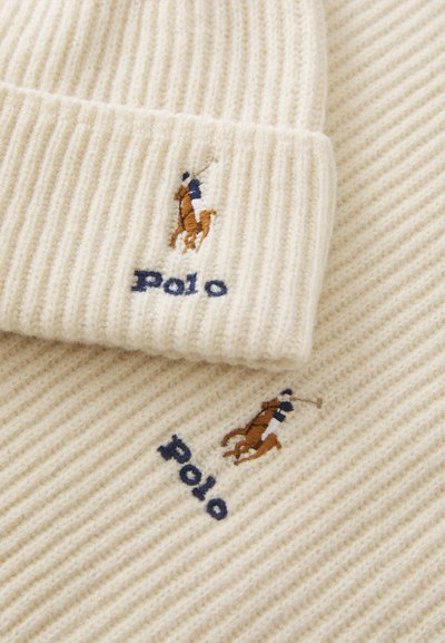 Kremfarget ribbestrikket lue- og skjerfsett, med brodert hest og rytterlogo i brunt og blått, med "Polo" i marineblått under.