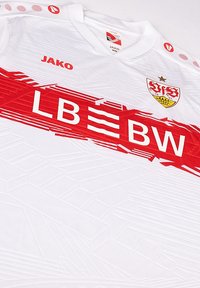 Maglia sportiva bianca con una striscia diagonale rossa e un design texture. Presenta il testo "LB BW" e un logo della squadra con una stella e uno scudo.
