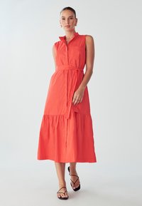 Koralen brezrokavnik s ovratnikom, z pasom na višini pasu, z večplastnim dnom. Narejen iz lahkotnega materiala, dolžina do gležnjev, z enostavnim dizajnom.