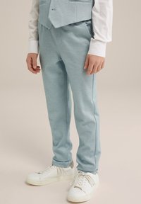 Heledad sinised dressipüksid, millel on sile tekstuur, kitsenev disain ja küljetaskud, kombineeritud valgete tennisekingadega, millel on tekstureeritud tald.