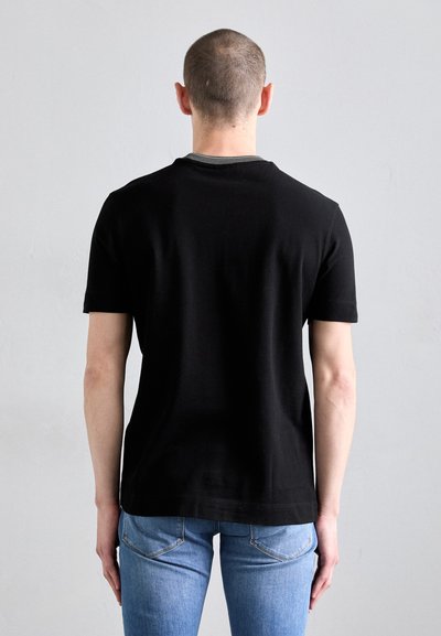 T-shirt noir à manches courtes avec un design classique à col rond, coupe ajustée, fabriqué en coton. Porté avec un jean bleu clair, montrant des détails minimes.