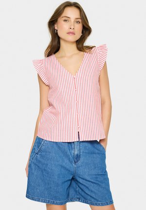 Röd och vit randig linne utan ärmar med V-ringning, volangärmar och framknappar, matchat med denimshorts.