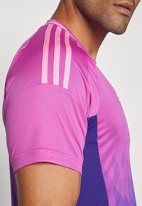 Camiseta atlética de manga corta con un diseño degradado en rosa y morado, y tres rayas contrastantes en rosa en el hombro.