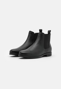 Bottes Chelsea en cuir noir avec panneaux latéraux élastiques, bouts arrondis et languettes, présentant une texture lisse et des talons blocs bas.