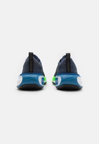 O pereche de adidași Nike de culoare albastră și verde, văzuți din spate, având buclele negre pentru călcâi și talpa groasă cu amortizare.
