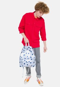 Zaino blu traslucido con pois navy, in tessuto, dotato di spallacci doppi, tasca frontale e chiusura regolabile con cordino.