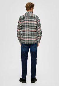Langsleeve geblokt overhemd in zwart, groen en wit met rode accenten, gemaakt van stof met een gladde textuur, gecombineerd met donkere denim jeans.
