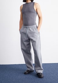 Szary top bez rękawów wykonany z gładkiej tkaniny w połączeniu z luźnymi szarymi dresami z elastycznym pasem oraz czarnymi trampkami.