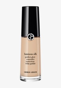 Il correttore Luminous Silk di Giorgio Armani in una bottiglia di vetro trasparente con un tappo nero e un logo argento, che mostra un liquido beige chiaro all'interno.