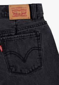 Jean en denim noir avec détail de poche arrière cousue, logo onglet rouge et étiquette de marque en cuir. Comprend un design classique à cinq poches et des rivets.