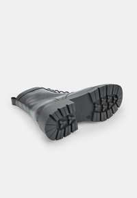 Stivale alla caviglia in pelle nera con suola in gomma robusta, parte superiore texturizzata e tacco rinforzato. Presenta lacci e un tassello sul retro.