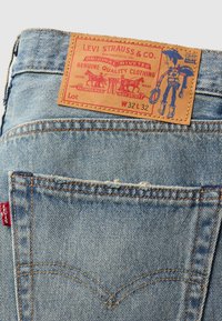 Jasnoniebieskie dżinsy z denimu z skórzaną metką z grafiką kowboja, detalami szwów i czerwonym logo Levi's na tylnej kieszeni.
