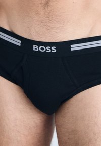 Zwarte katoenen boxershorts met een grijze elastische tailleband met het "BOSS" logo en twee horizontale grijze strepen. Glad textuur, klassieke pasvorm.