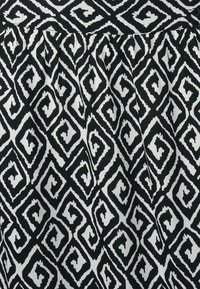 Černobílá látka se geometrickým vzorem vzájemně propojených diamantů a spirál, s texturovaným povrchem a nařasenými detaily.