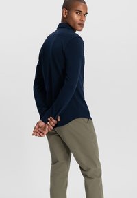 Marineblaues Langarm-Polohemd mit Kragen, figurbetonter Passform und geknöpften Manschetten, kombiniert mit hellolivgrünen Hosen.