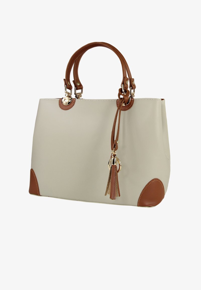 Sac fourre-tout beige avec des accents marron, y compris les poignées et des renforts aux coins. Dispose de ferrures dorées et d'un détail décoratif en forme de pompon. Texture lisse.