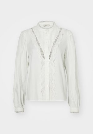 White blouse with gathered sleeves, vertical pleats, and lace trim along the placket. Features button closure and decorative cuffs.