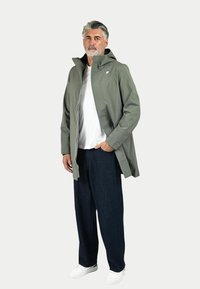 Svetlo siva nepremočljiva jakna s kapuco in zadrgo; v kombinaciji z belim majico, temno jeans hlačami in belimi športnimi čevlji.