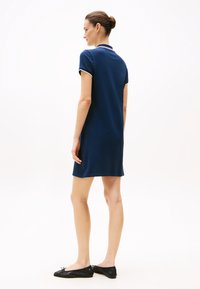 Laivastonsininen polo-mekko lyhyillä hihoilla, ribattua kaulusta, jossa valkoisia yksityiskohtia, suora leikkaus ja polven ylle ulottuva pituus. Päällä mustat ballerinat.