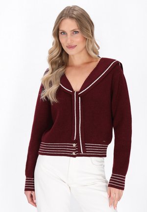 Burgundy neulecardigan, jossa on merimieskaulus, valkoiset raidat ja kolme nappia vyötäröllä. Pehmeä tekstuuri, rento malli.