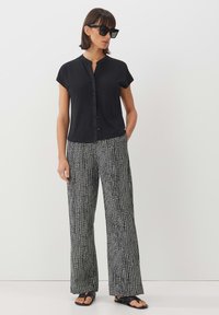 Black short-sleeve button-up shirt paired with loose-fitting black and white grid-patterned trousers and flat black sandals.