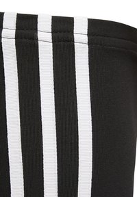 Tessuto nero con righe bianche verticali. Il materiale ha una trama a coste e presenta cuciture evidenti lungo i bordi delle righe.