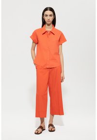 Bright orange two-piece outfit featuring a short-sleeve button-up shirt and wide-leg cropped pants. Includes a tie detail at the collar.