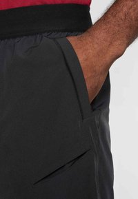 Calções pretos com cintura elástica, bolso lateral e tecido leve e suave com acabamento mate.