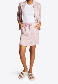 Blazer rosa a fantasia abbinato a una mini gonna con coulisse. La gonna presenta un tessuto testurizzato e una coulisse rosa. Indossato con sandali beige.