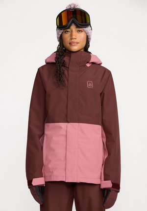 Veste de snowboard bordeaux et rose avec fermeture éclair, capuche et détail de logo. Présente des poignets texturés et un design en blocs de couleur.