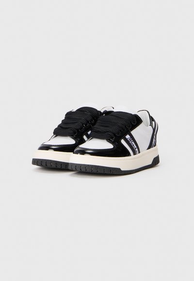 White and black sneakers with thick black laces, thick white soles, and branding on the side panels and back tabs.