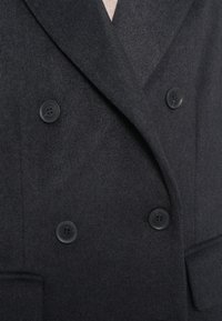 Cappotto in misto lana grigio scuro con doppio petto, dotato di bottoni neri e rever a punta. Tessuto testurizzato con tasche laterali.