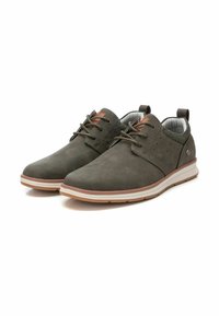 Zapatos de color verde oscuro con un empeine texturizado, punta redonda y suela blanca contrastante. Cuentan con cordones, pequeños acentos laterales y una lengüeta en el talón.