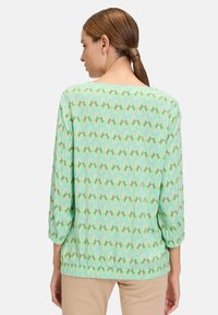 Top verde con motivo, maniche a tre quarti, realizzato in tessuto leggero, con scollo rotondo e vita elasticizzata per una vestibilità comoda.