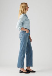 Ljusblå denimskjorta med knäppning, kombinerad med högmidjade, något utsvängda blå jeans. Svarta platta skor fulländar outfiten.