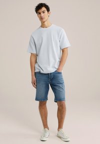 Ljusblå kortärmad t-shirt, matchad med blå denimshorts och vita sneakers. Enkel, avslappnad passform med en mjuk textur.