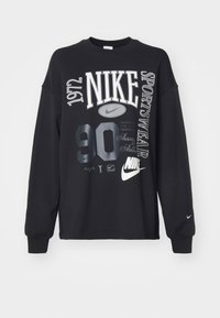 Svart Nike sweatshirt med rund halsringning. Har stor vit och grå text, inklusive "1972", "NIK" och "90". Långa ärmar med logodetalj.