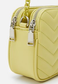 Borsa a tracolla gialla in pelle con motivo a zigzag, doppie cerniere in argento e dettagli a catena, caratterizzata da una superficie liscia e una forma compatta.