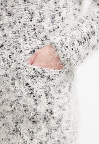 Luddig, texturerad tröja i vitt och grått med fickdetalj. Har långa ärmar och ett mjukt, mysigt utseende.