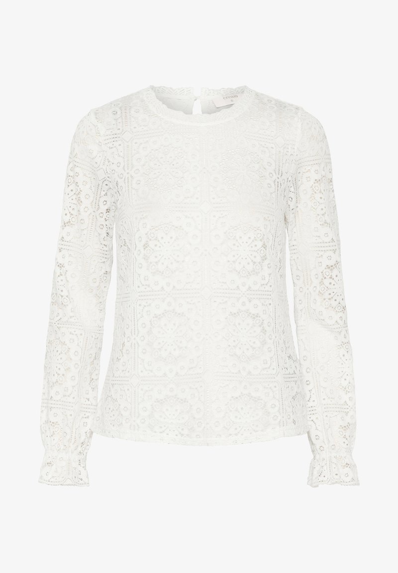 Blouse blanche à manches longues en dentelle avec motifs floraux et géométriques, encolure ronde, fermeture par bouton en forme de gouttière à l'arrière, et poignets légèrement froncés.