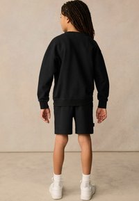 Černý bavlněný set mikiny a šortek, ležérní design, žebrované manžety, volný střih, doplněný o bílé tenisky a kotníkové ponožky.