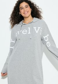 Harmaa hupullinen pitkähihaisen collegepaita, jossa valkoisella painettu "Travel Vibe" -teksti. Pehmeä materiaali ja rento istuvuus.