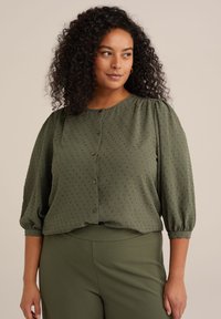Blusa verde oliva in tessuto testurizzato, colletto rotondo, chiusura con bottoni e maniche a palloncino. Abbinata a pantaloni verdi coordinati.