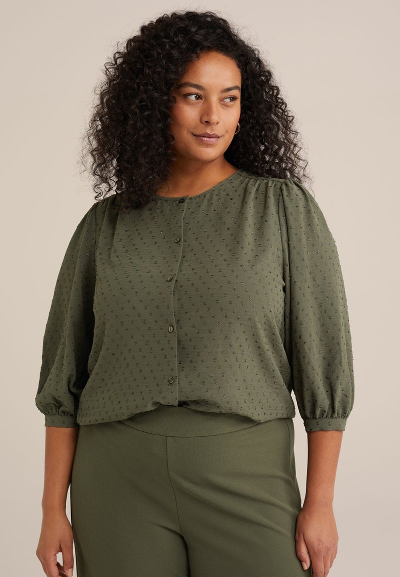 Blusa verde oliva in tessuto testurizzato, colletto rotondo, chiusura con bottoni e maniche a palloncino. Abbinata a pantaloni verdi coordinati.