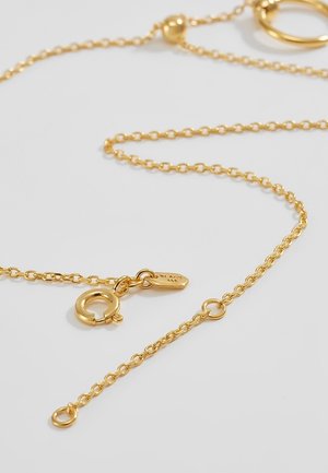 Goldene Halskette mit FEDERRING-Verschluss und kleinem rechteckigen Anhänger vor einfachem hellem Hintergrund.