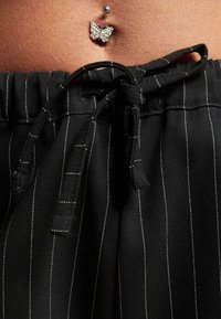 Čierne pruhované nohavice s pružným pásom. Obsahujú dekoratívny piercing v pupku vo forme motýľa s rhinestones.