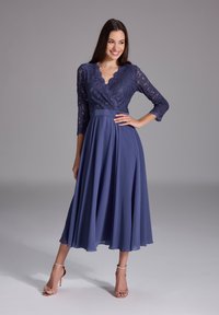 Un abito blu navy con corpetto in pizzo, scollatura a scallop e maniche a trequarti, e una gonna in chiffon plissettata e fluida.