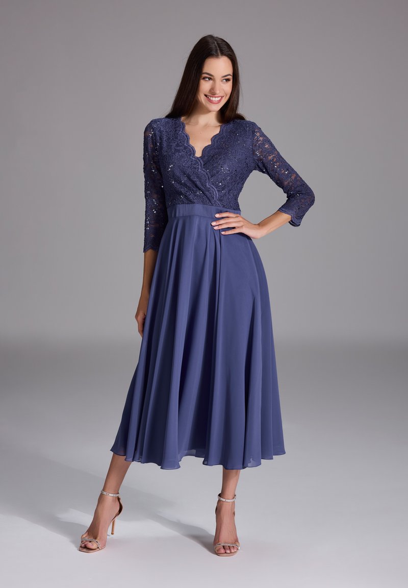 Navy blue dress with a lace bodice that has a scalloped neckline and three-quarter sleeves, adorned with a flowing, pleated chiffon skirt.